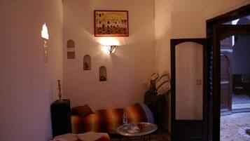 Uma sala de estar acolhedora com um sofá, uma mesinha com um copo e uma porta que dá para um pátio.
