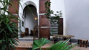 A courtyard with a round table, chairs, and potted plants. - Riad Felloussia (Meknes)