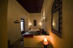 A dimly lit room with a bed, a small table, and a wall-mounted mirror.