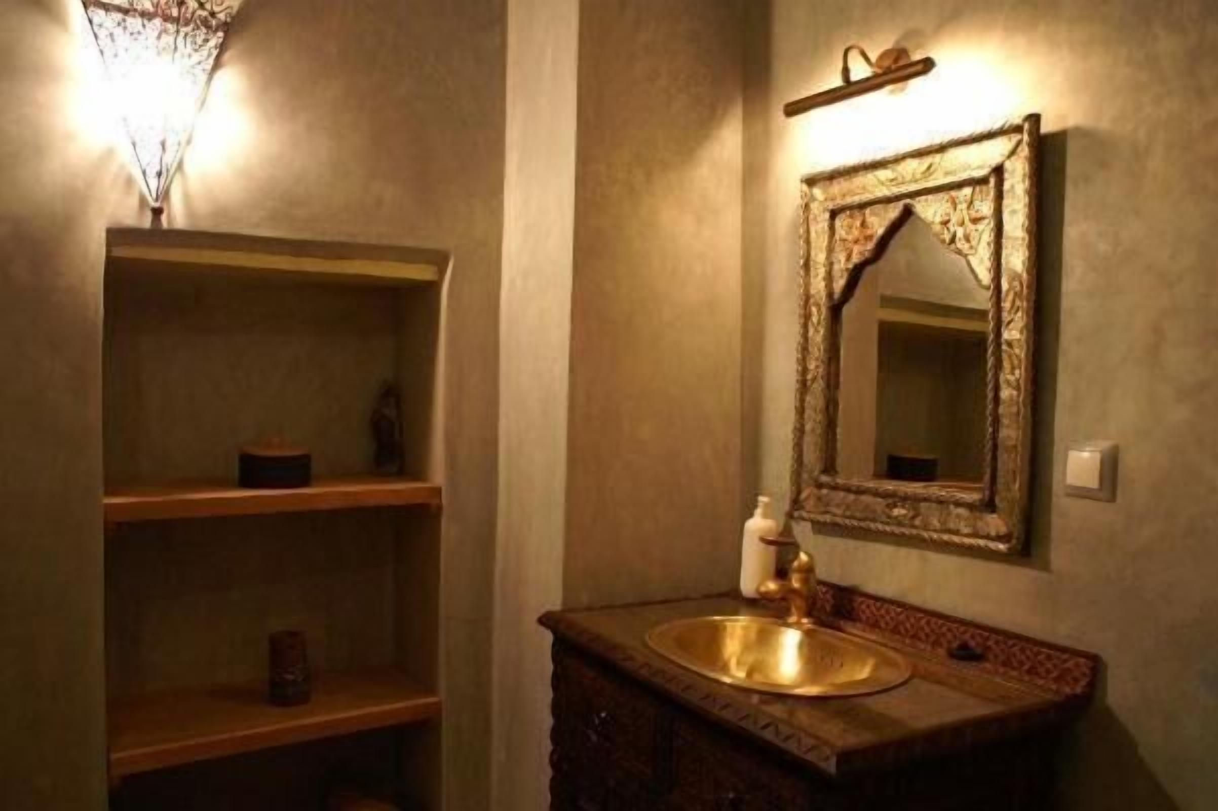 Ein Badezimmer mit einem Holzbadezimmerhocker, einem goldfarbenen Waschbecken und einem Spiegel mit aufwendiger Rahmung.