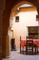 An interior with a stone archway, a wooden chair with a pink tablecloth, and a cabinet with glass doors.