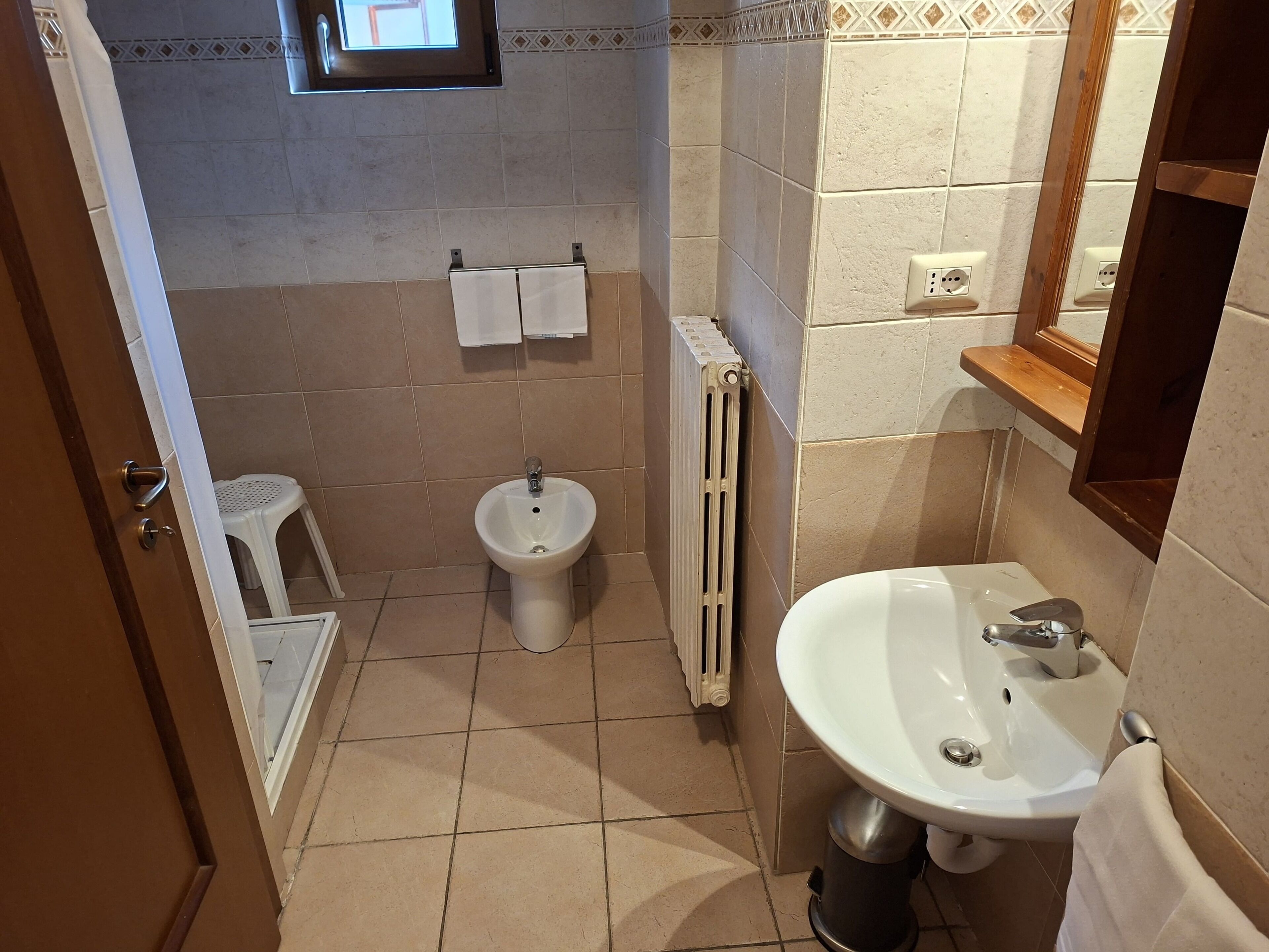 A bathroom with a pedestal sink, a bidet, a toilet, and a window above the sink.