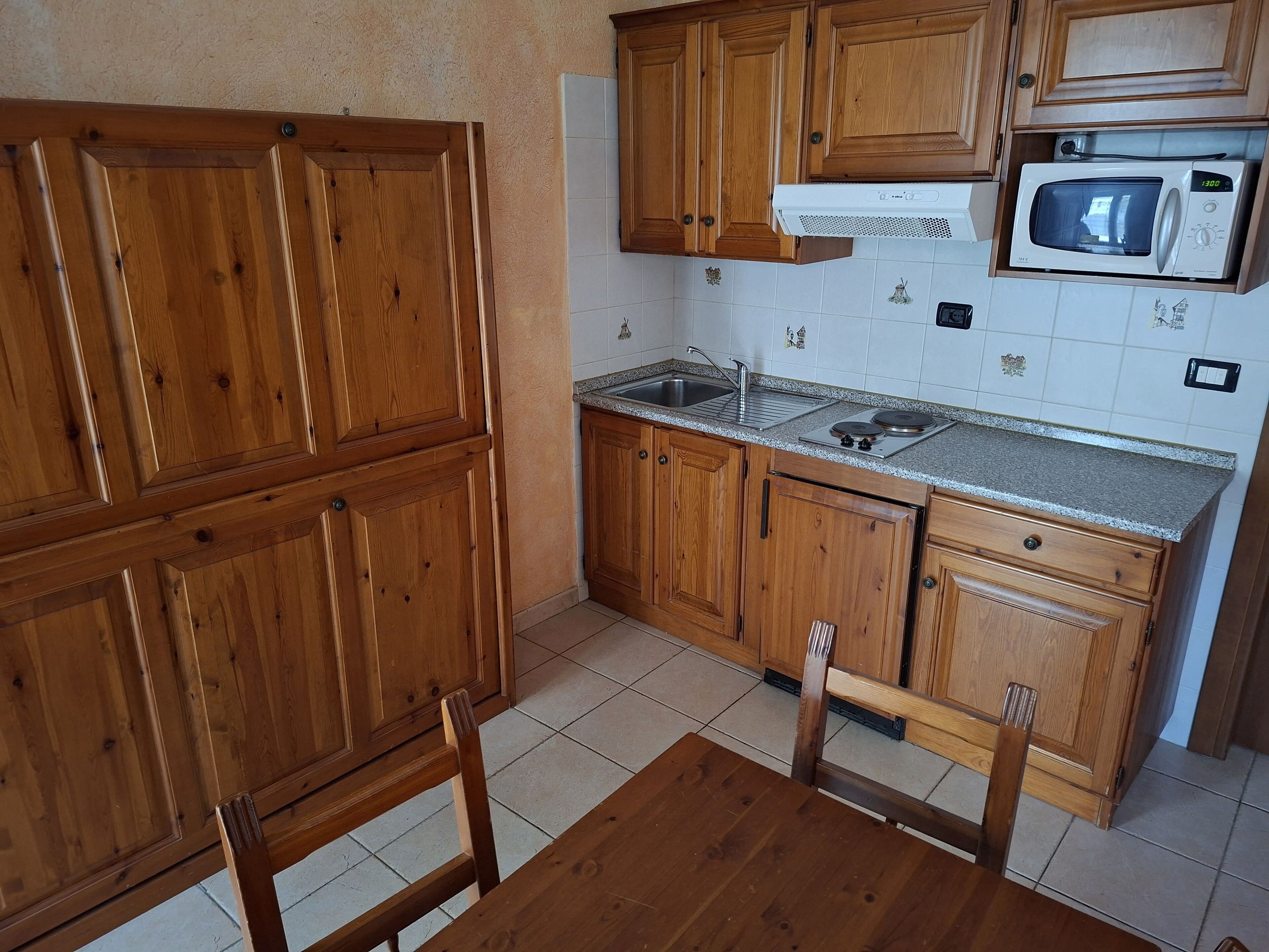 A kitchen with wooden cabinets, a microwave, a sink, and a dining table with chairs.