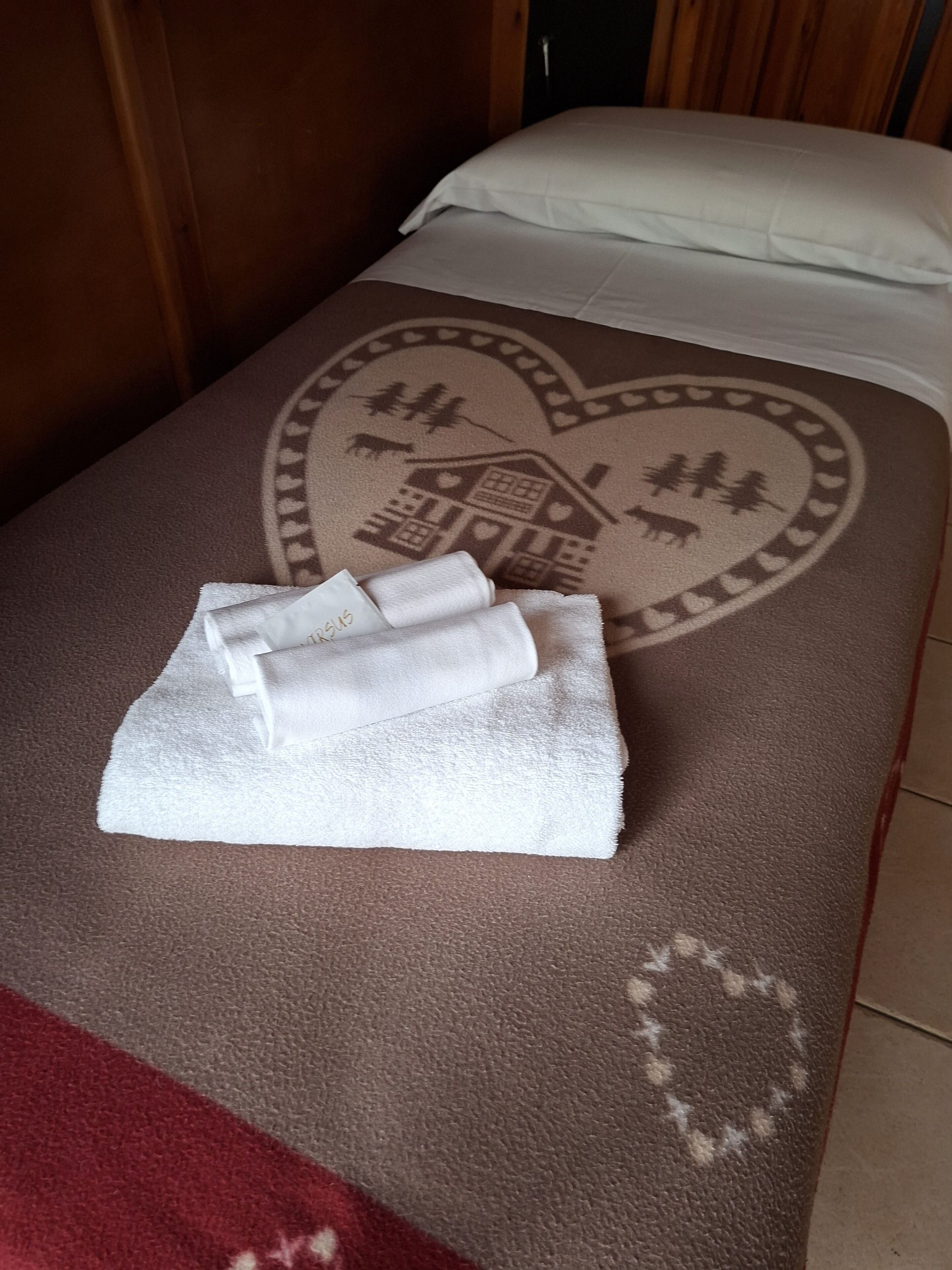 A bed with a heart-shaped design, a folded white towel, and a red and brown textured blanket.