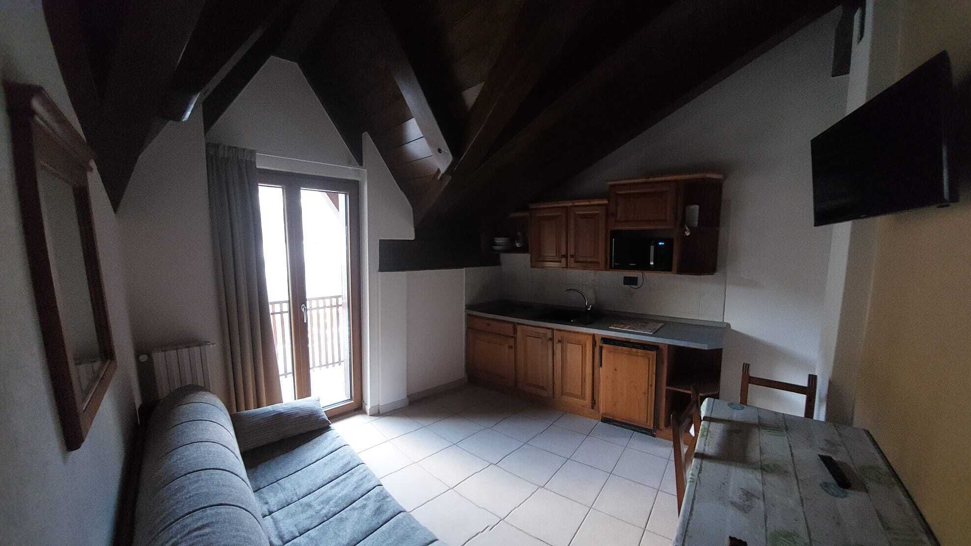 A cozy living room with a sofa, a dining table, and a kitchen area with wooden cabinets and a microwave.