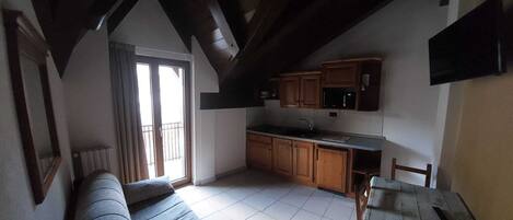 A cozy living room with a sofa, a dining table, and a kitchen area with wooden cabinets and a microwave.