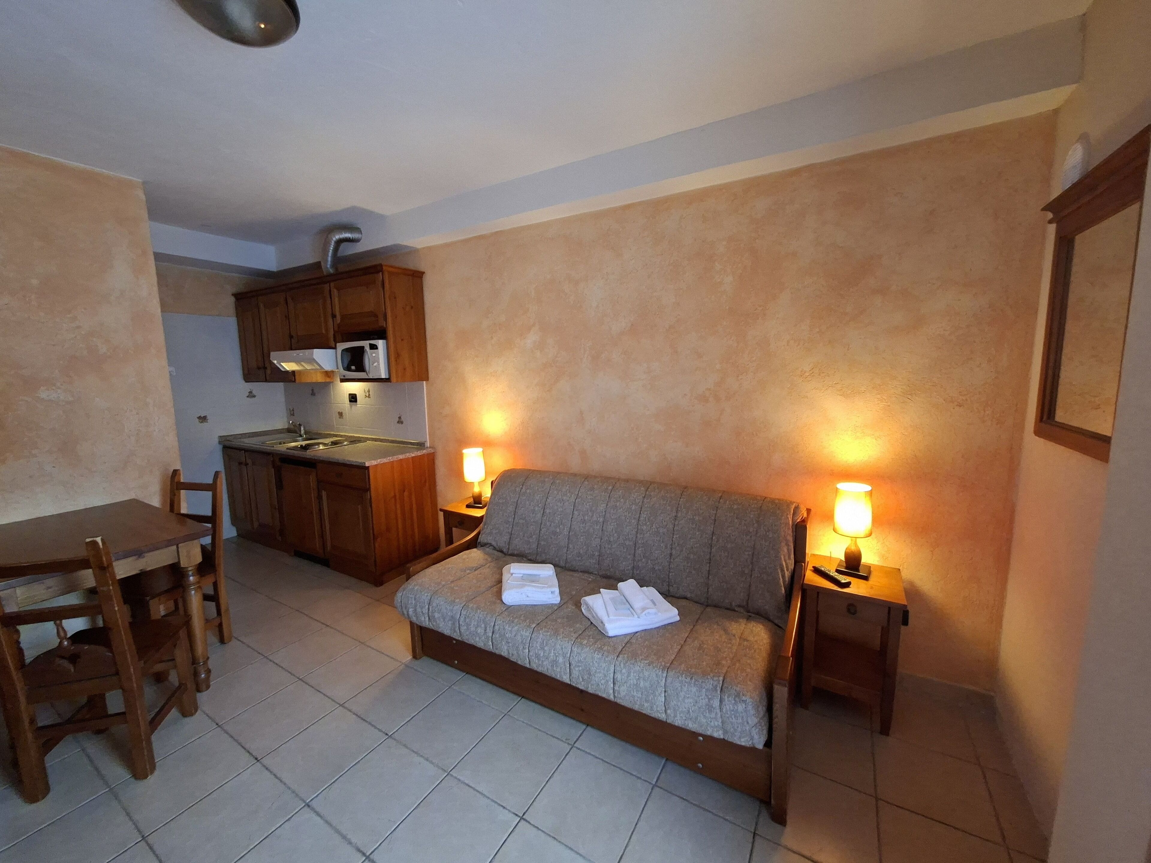 A compact living space with a kitchenette, a sofa with a blanket, and two bedside lamps.