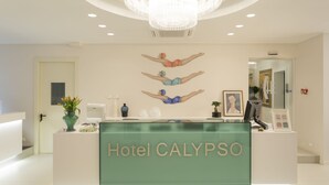A hotel reception desk with a modern design, a chandelier, and artwork on the wall. - Hotel Calypso (Rimini)
