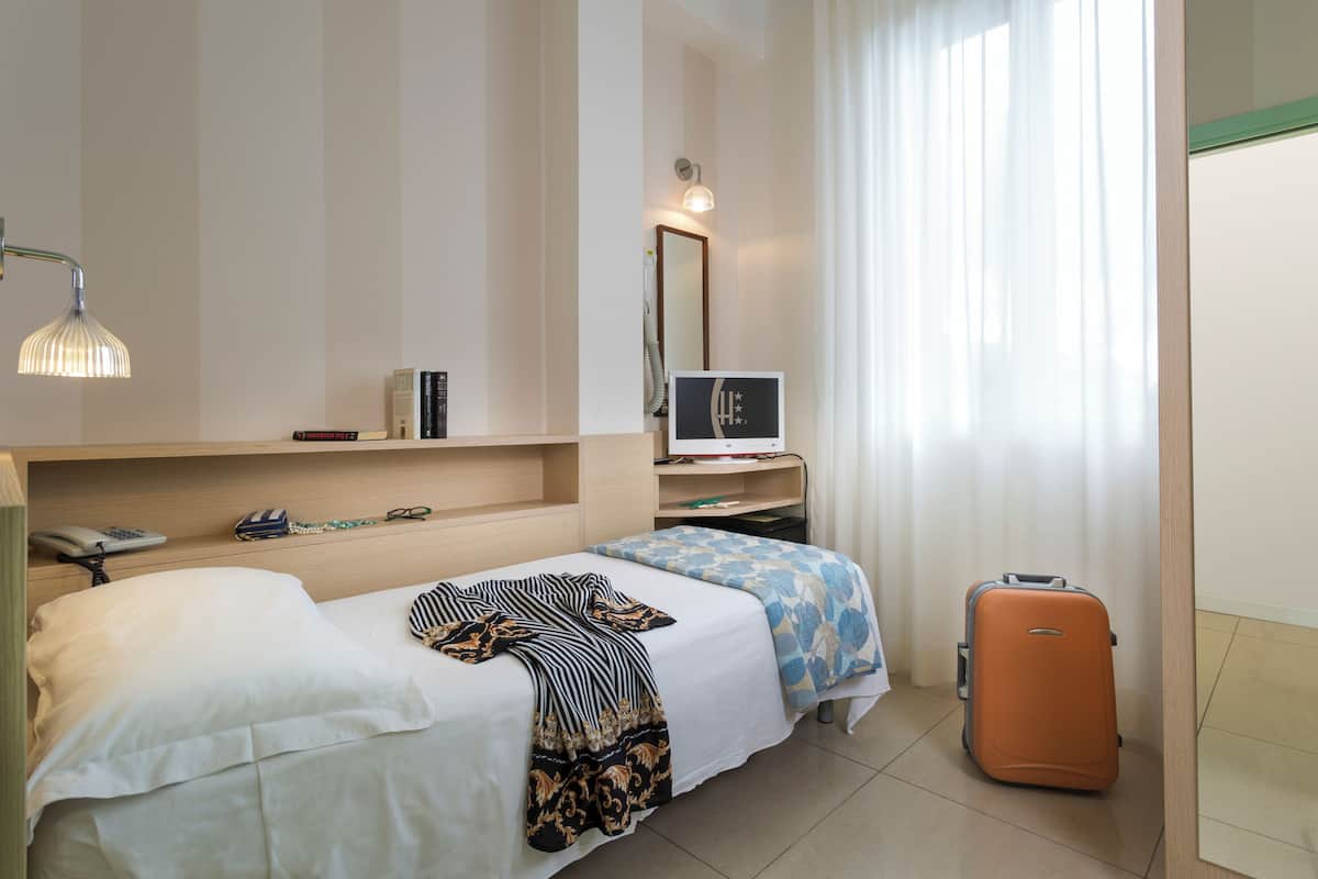 A hotel room with a bed, a desk with a computer, a suitcase, and a window with curtains.