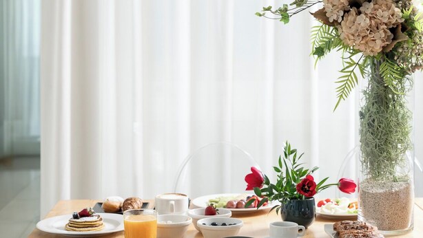 A breakfast setting with a wooden table, clear chairs, and a vase of flowers. - Hotel Calypso (Rimini)