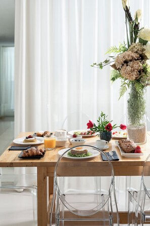 A breakfast setting with a wooden table, clear chairs, and a vase of flowers. - Hotel Calypso (Rimini)