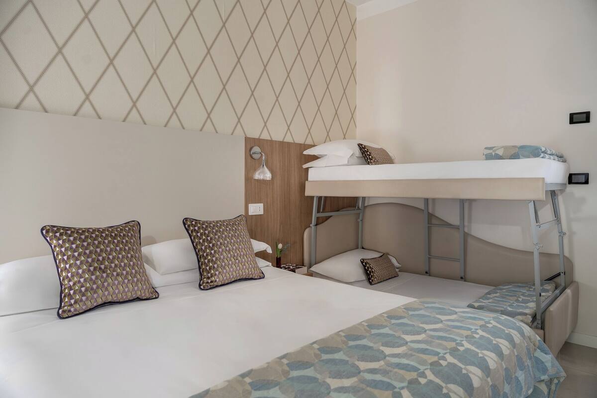 A bunk bed room with a patterned wall, a bedside table with a lamp, and a patterned bedspread.