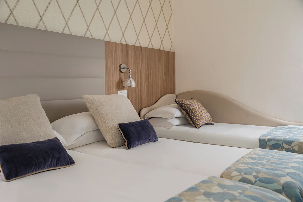 A hotel room with a modern design, featuring a large bed with multiple pillows and a headboard with a built-in lamp.