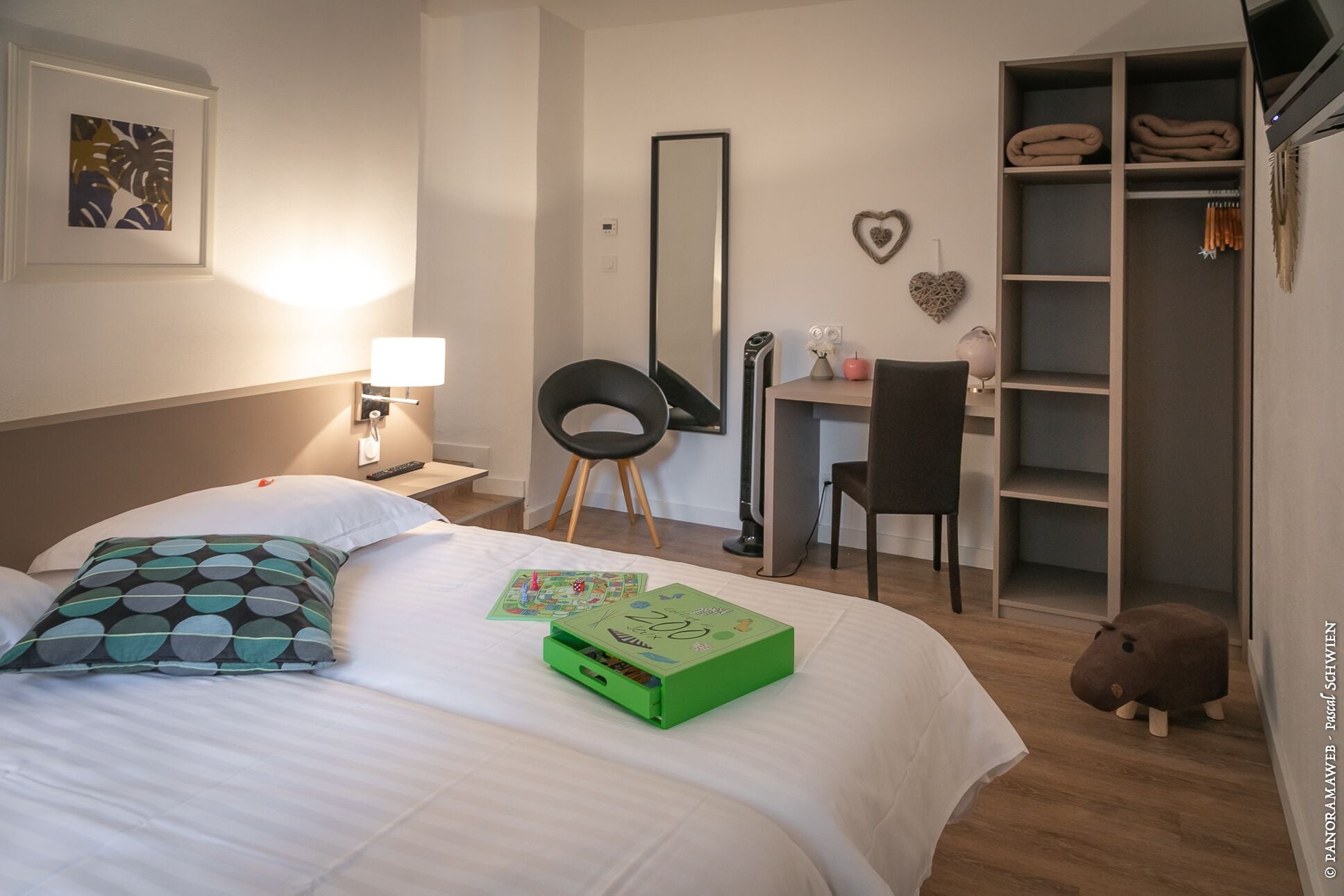 Hotellihuone, jossa on sänky, työpöytä, tuoli, kirjahylly ja pehmolelu.