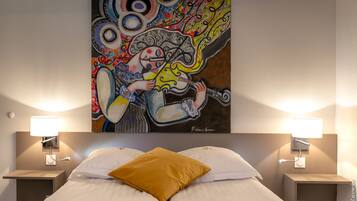 A hotel room with a bed, a nightstand, a lamp, and a colorful abstract painting on the wall.