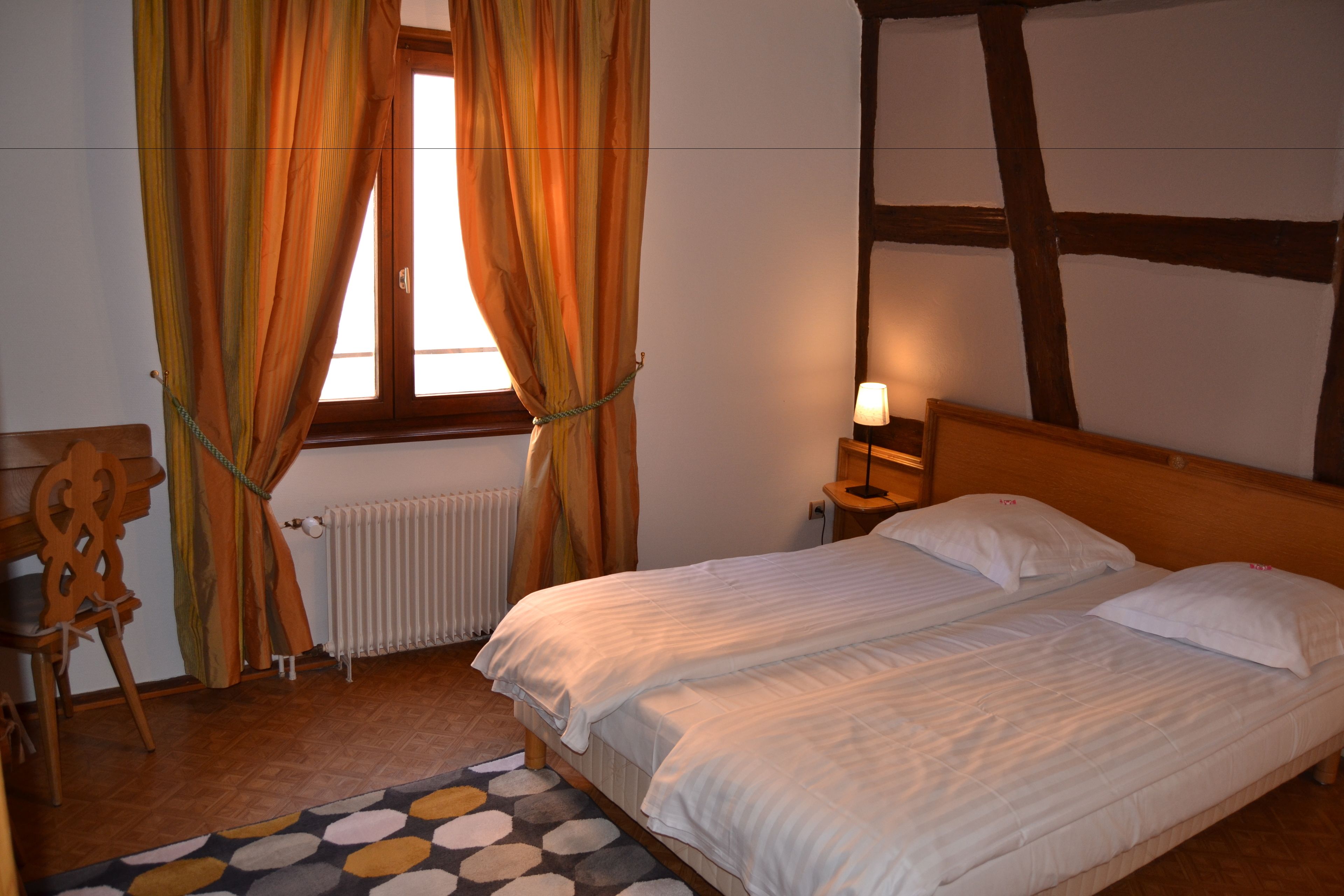 Une chambre à coucher avec un lit double, une tête de lit en bois, une table de chevet avec une lampe, une chaise et une fenêtre avec des rideaux.