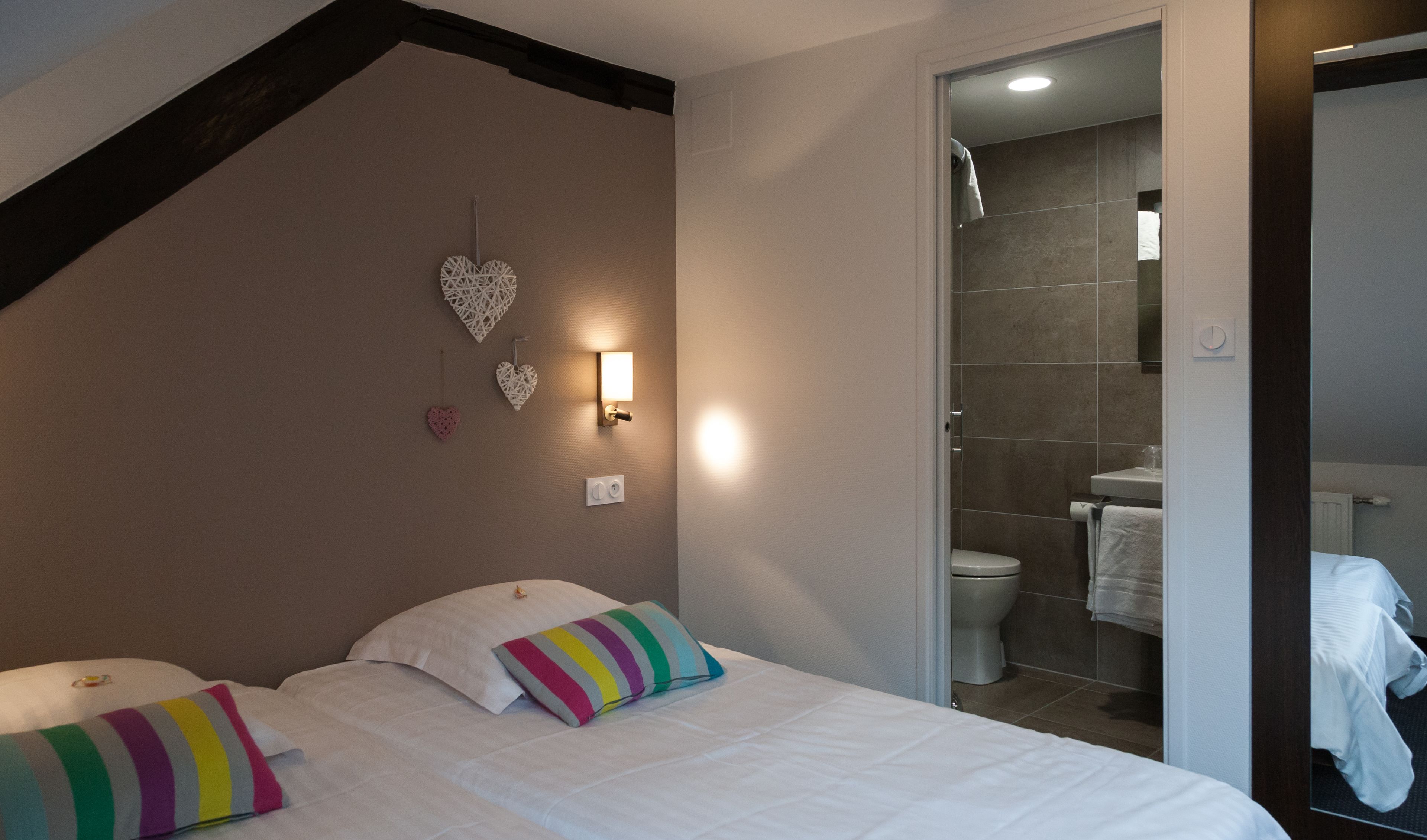 A bedroom with a bed, pillows, a wall-mounted light, and a bathroom visible through an open door.