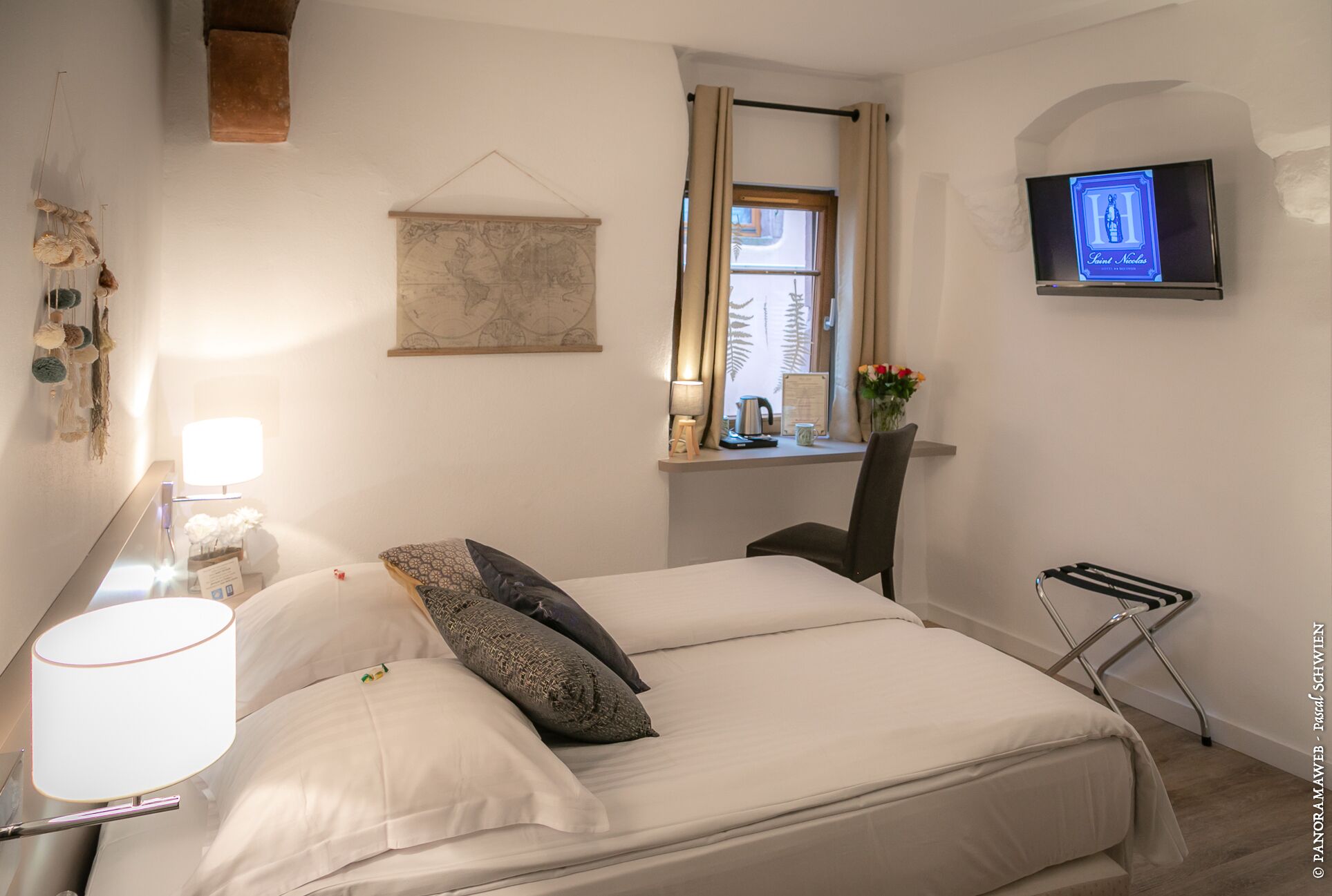 Ein Hotelzimmer mit einem Bett, einem Schreibtisch mit Lampe, einem Fernseher und einem Fenster mit Vorhängen.