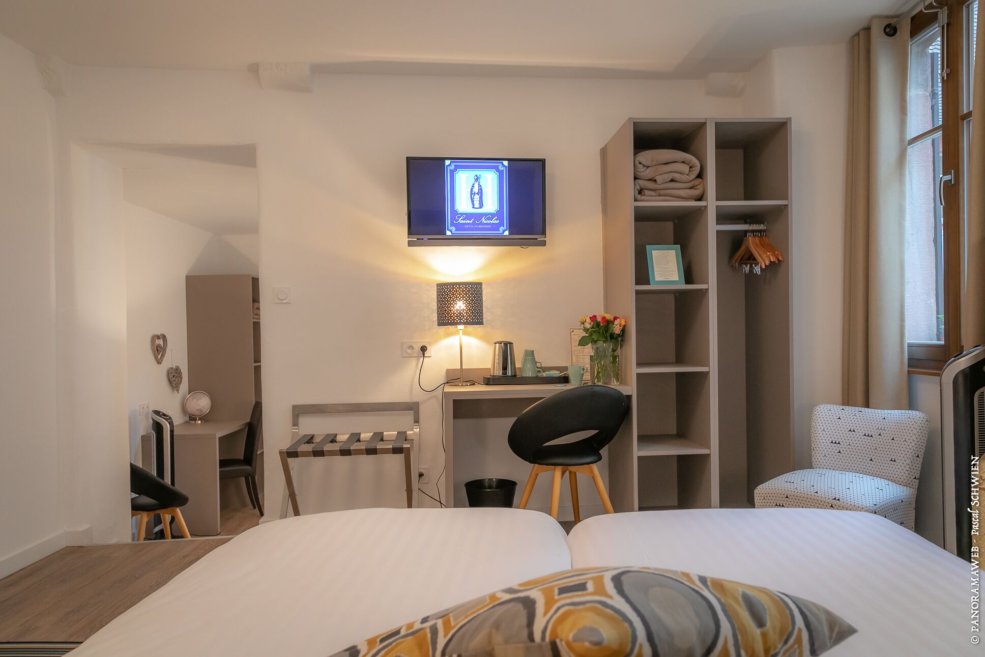 Ein Hotelzimmer mit einem Bett, einem Schreibtisch mit Computer, einem Sessel, einem an der Wand befestigten Fernseher und einem Kleiderschrank.