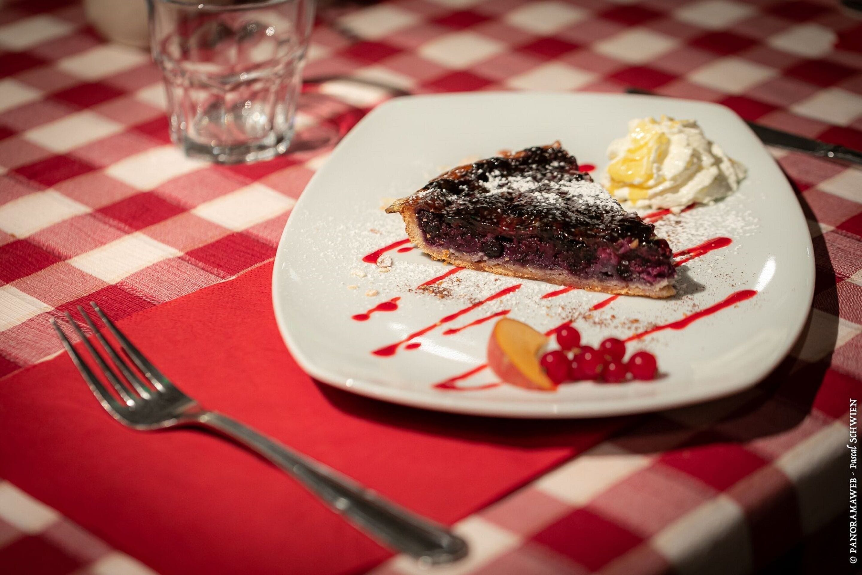 A dessert plate with a slice of pie and whipped cream on a checkered tablecloth.
