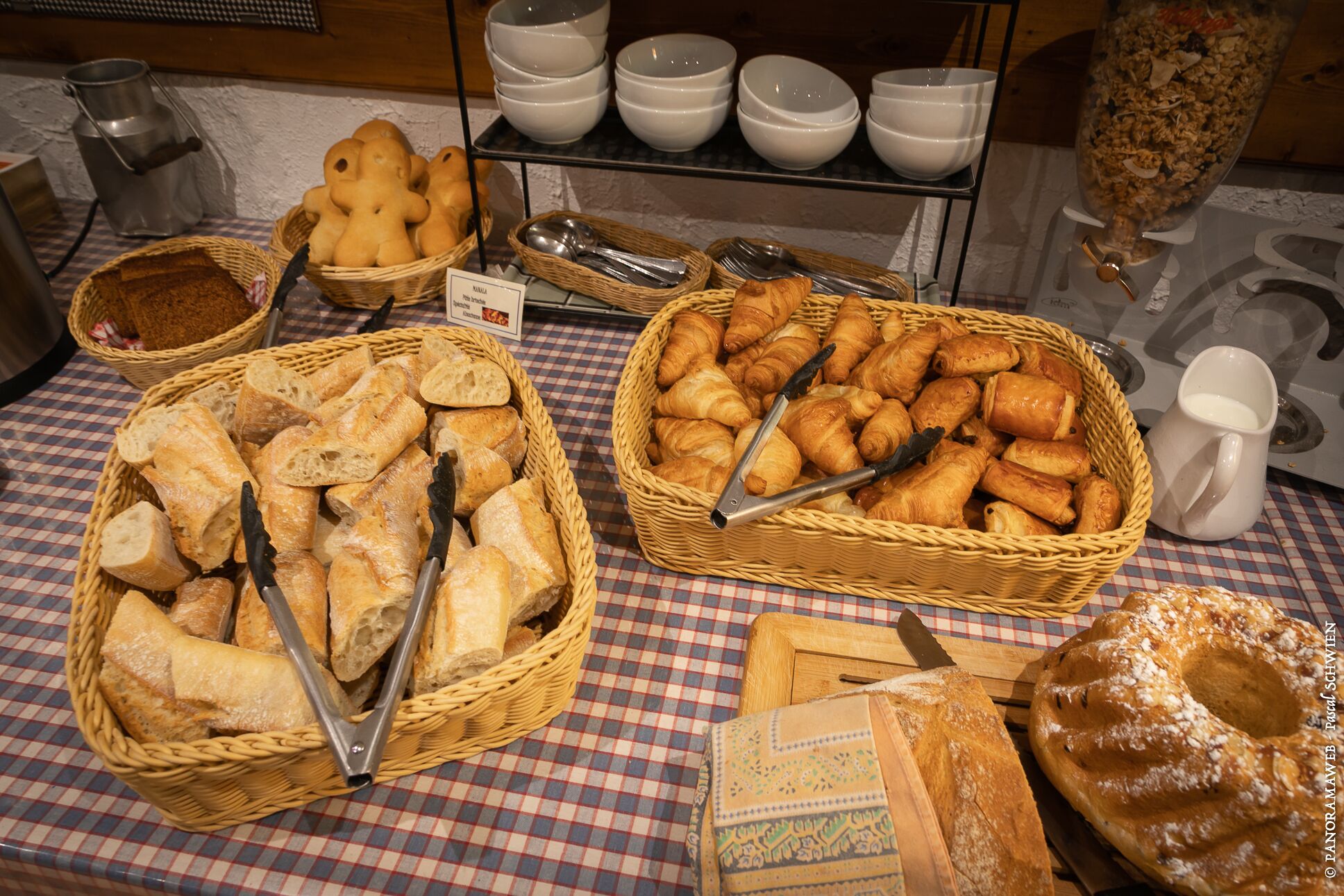 Uma mesa de buffet com diversos pães e doces, incluindo croissants e baguetes, dispostos em cestas.