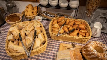 Una mesa de buffet con diversos panes y pasteles, incluyendo croissants y barras, dispuestas en cestas.