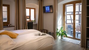 A hotel room with a bed, a TV, a window, a balcony with outdoor furniture, and a plant. - Hotel Restaurant Saint Nicolas (Riquewihr)