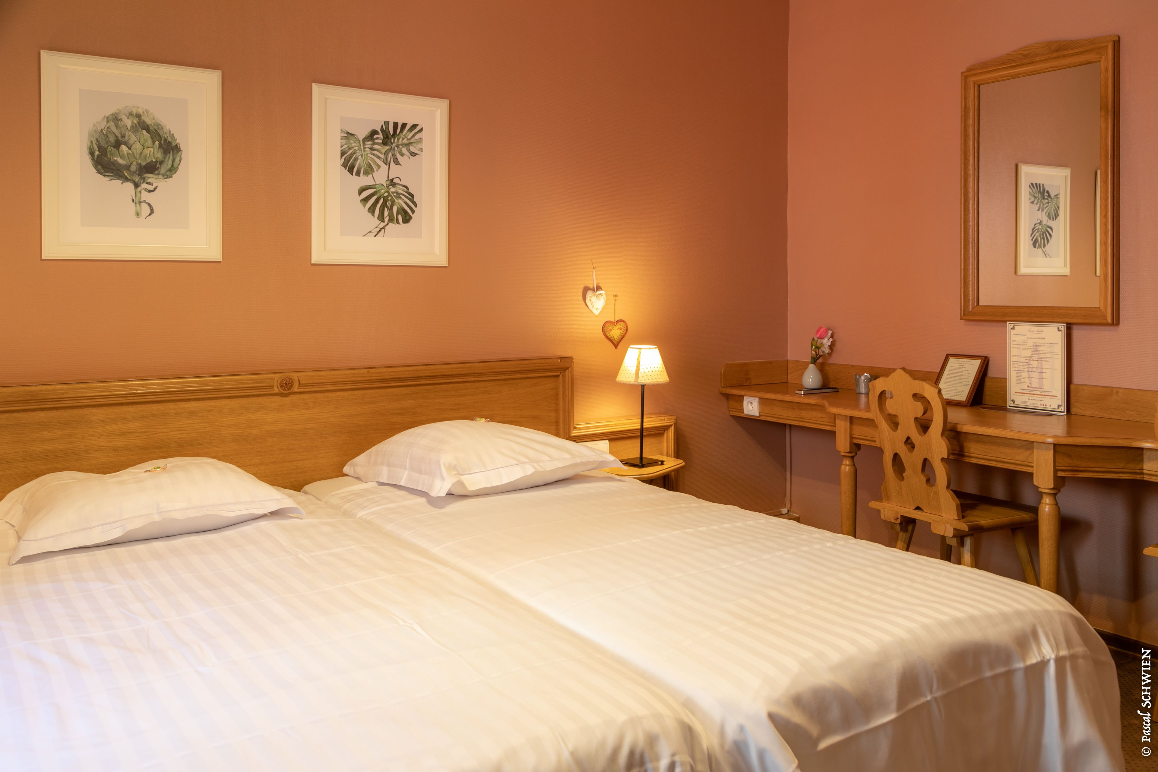 Une chambre d’hôtel avec deux lits, un bureau, une chaise et des œuvres d’art botanique encadrées accrochées aux murs.