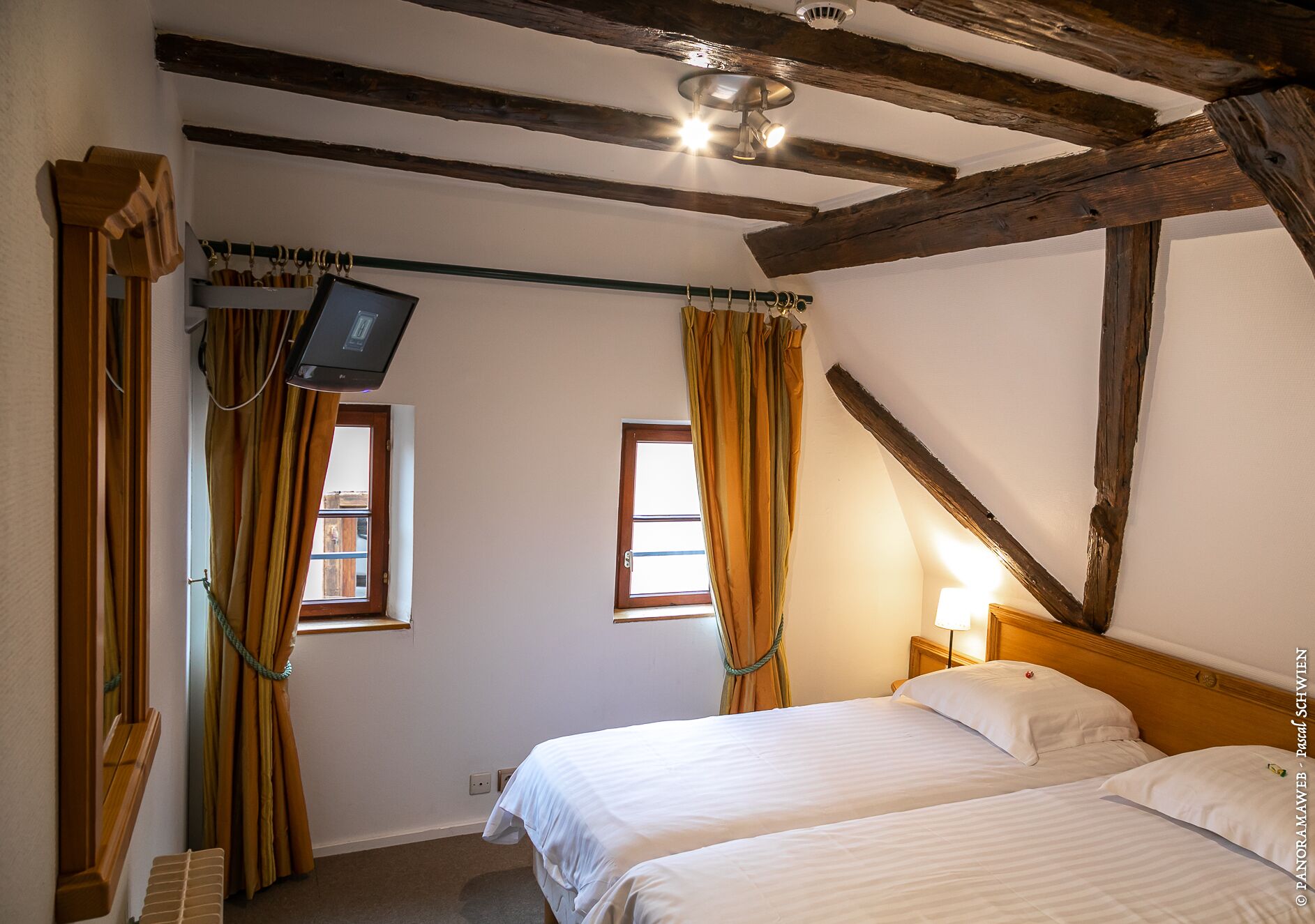 Une chambre avec deux lits, des poutres en bois, une télévision et des rideaux.