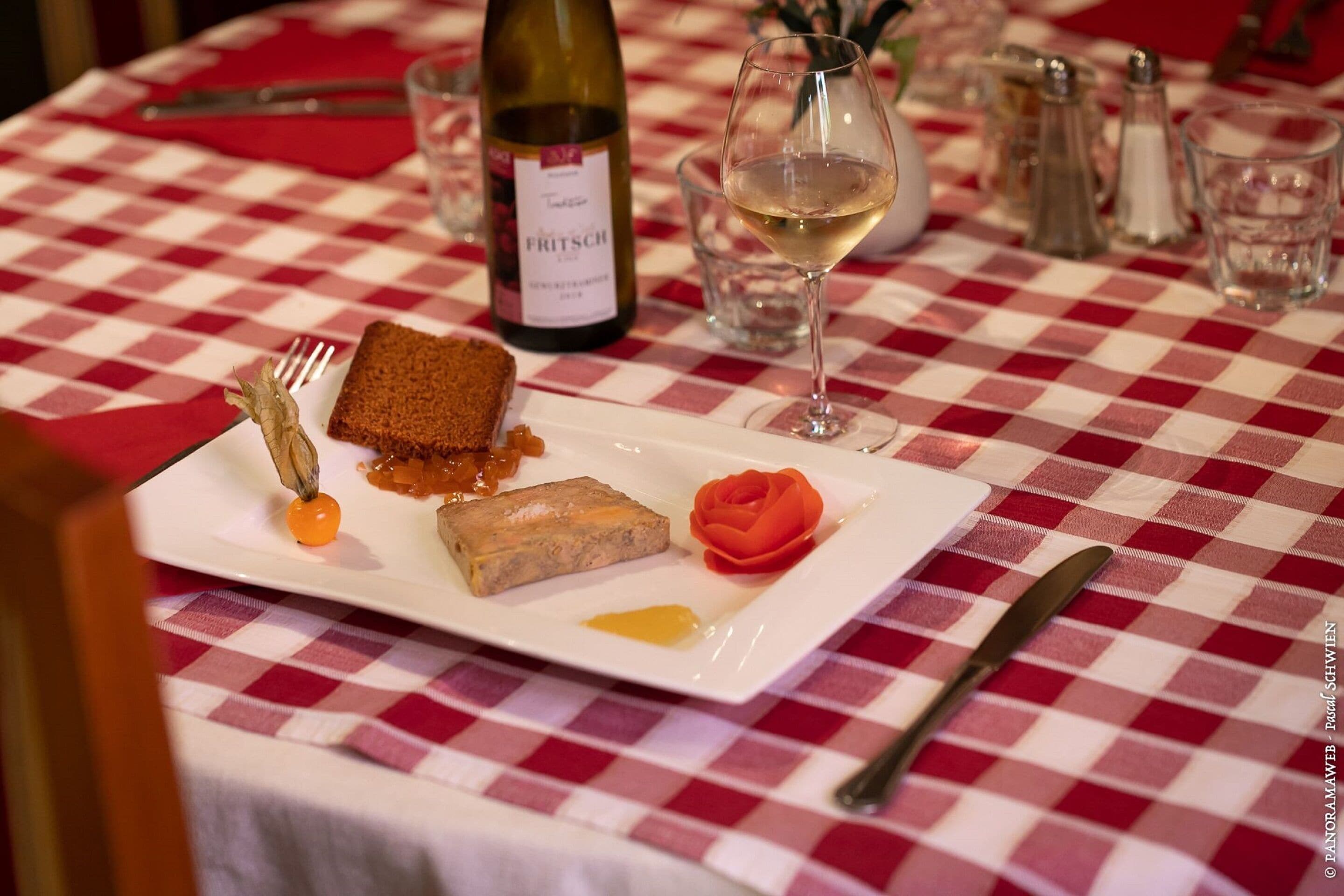 Una mesa de comedor con mantel a cuadros, una botella de vino, una copa de vino y un plato de comida.