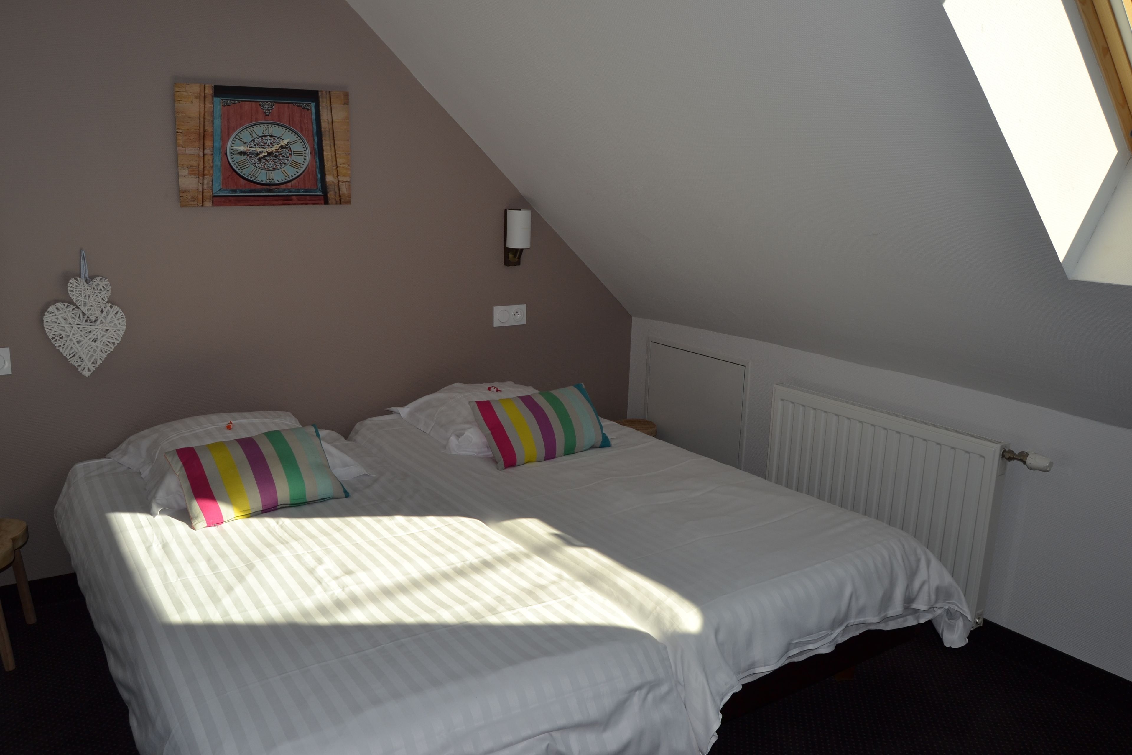 Un dormitorio con dos camas, un reloj de pared, una decoración con forma de corazón y una ventana que deja entrar luz natural.
