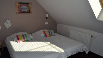 Un dormitorio con dos camas, un reloj de pared, una decoración con forma de corazón y una ventana que deja entrar luz natural.