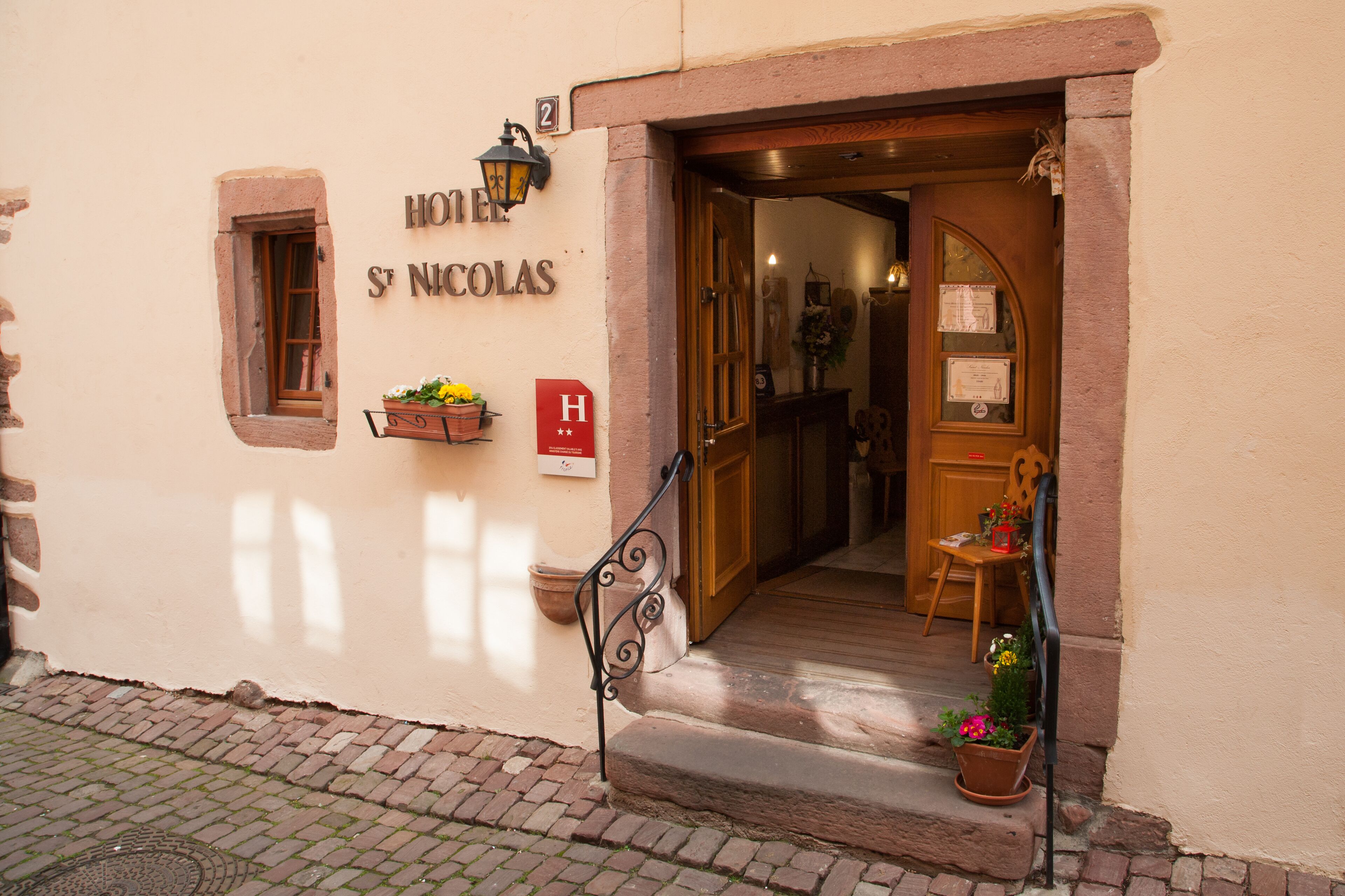 Entrada de un hotel con puerta de madera, una ventana pequeña y un cartel que dice "HOTEL ST NICOLAS".