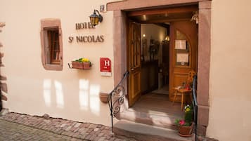Entrada de un hotel con puerta de madera, una ventana pequeña y un cartel que dice "HOTEL ST NICOLAS".