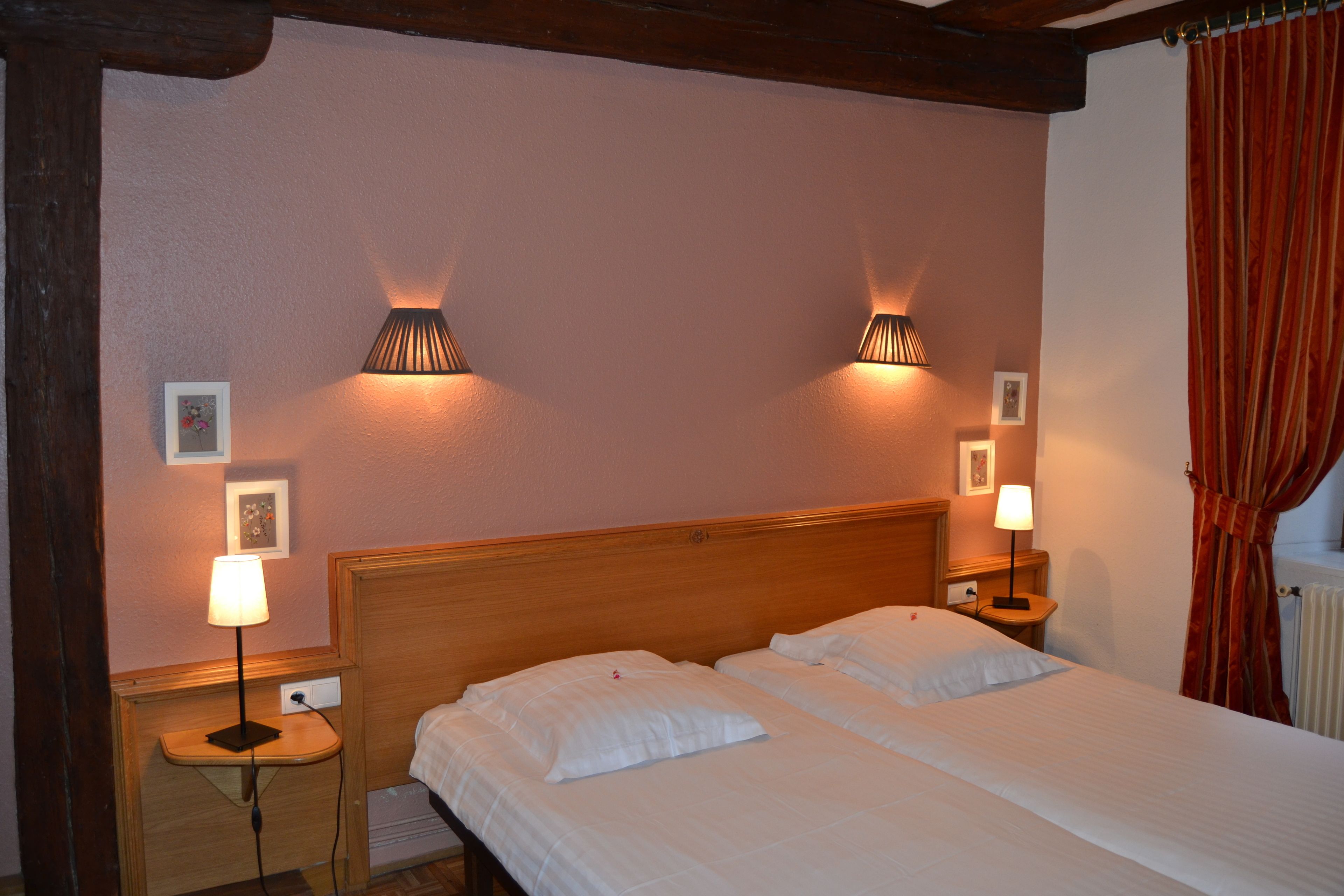 Een hotelkamer met twee bedden, houten hoofdeinden, bedlampen en ingelijste foto’s aan de wand.
