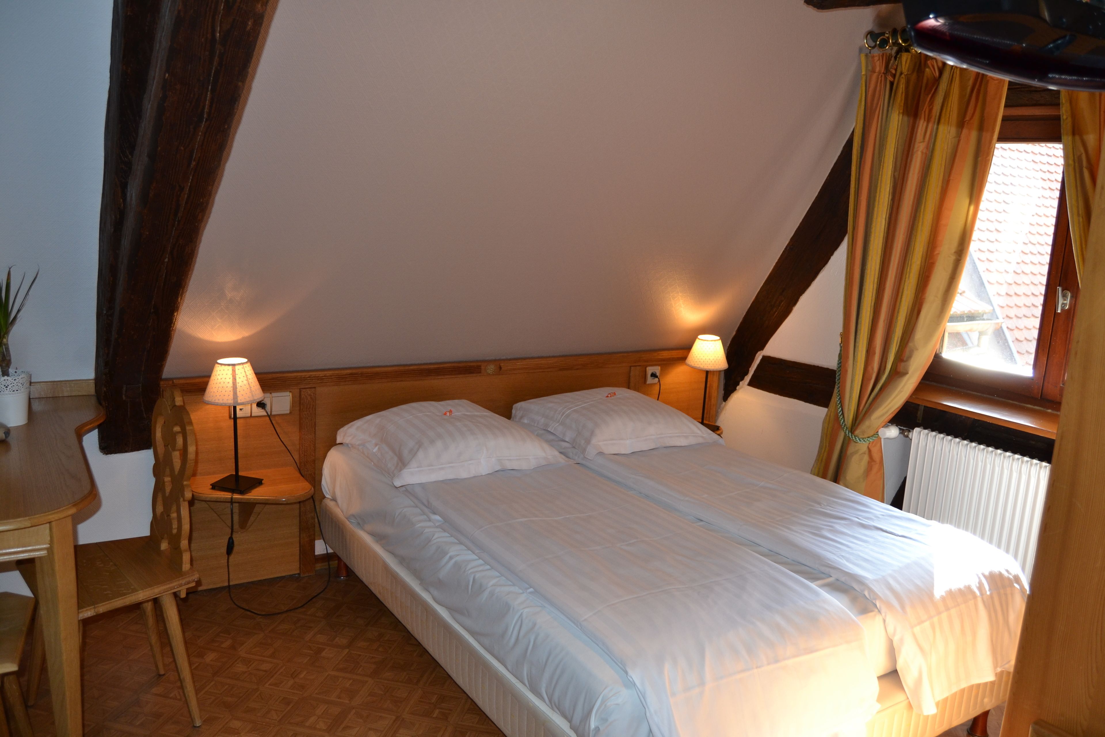 A bedroom with two beds, a wooden desk, and lamps.