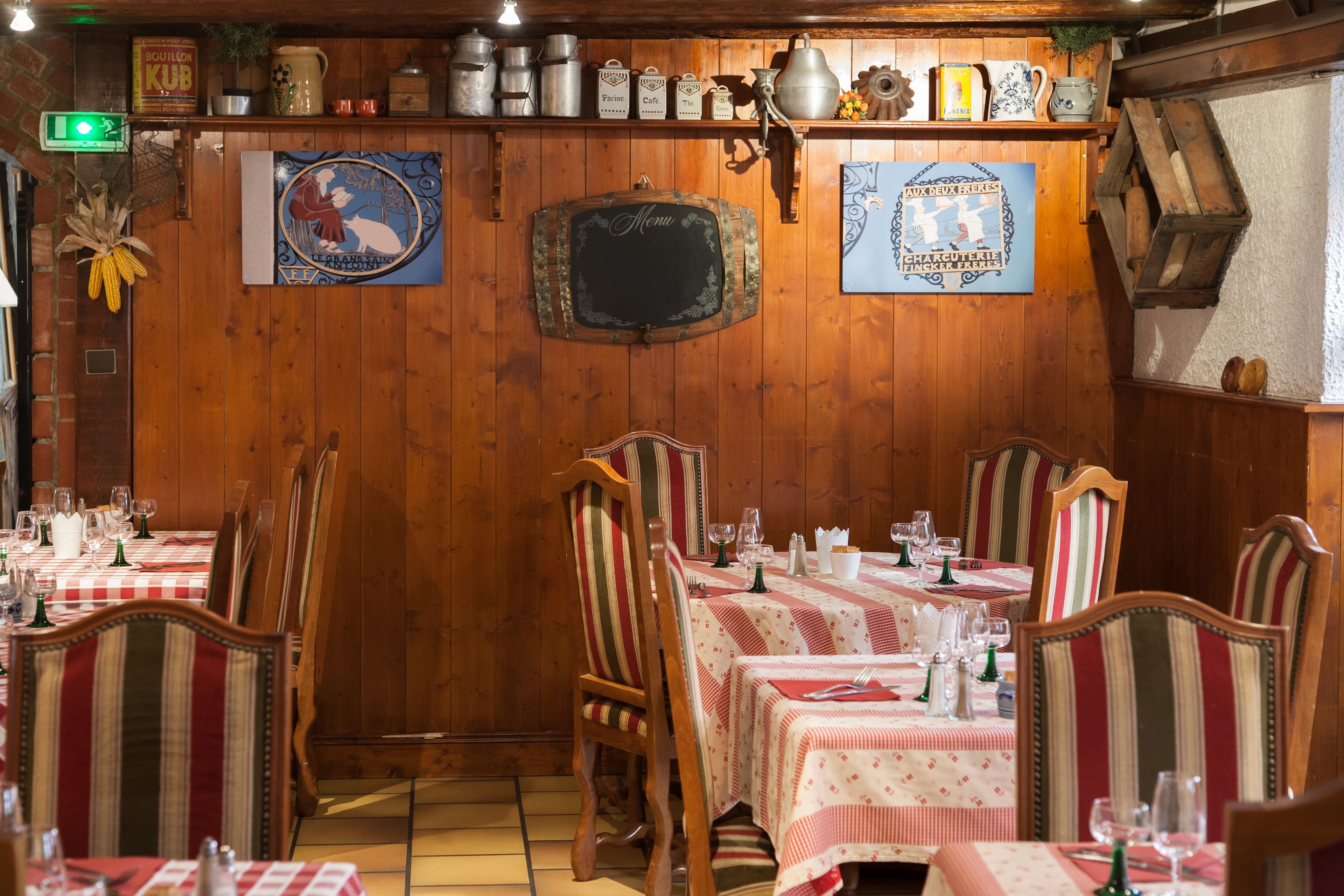 A restaurant with wooden walls, striped chairs, and tables set with red and white checkered tablecloths.