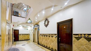 Um hall de hotel com piso de mármore, uma grande porta de madeira e um vitral.