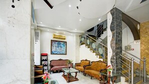 Um hall com piso de mármore, dois sofás, uma mesa de centro de vidro e uma escadaria com corrimão de metal.