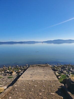 A calm lake with a clear sky, a distant sailboat, and a rocky shoreline.