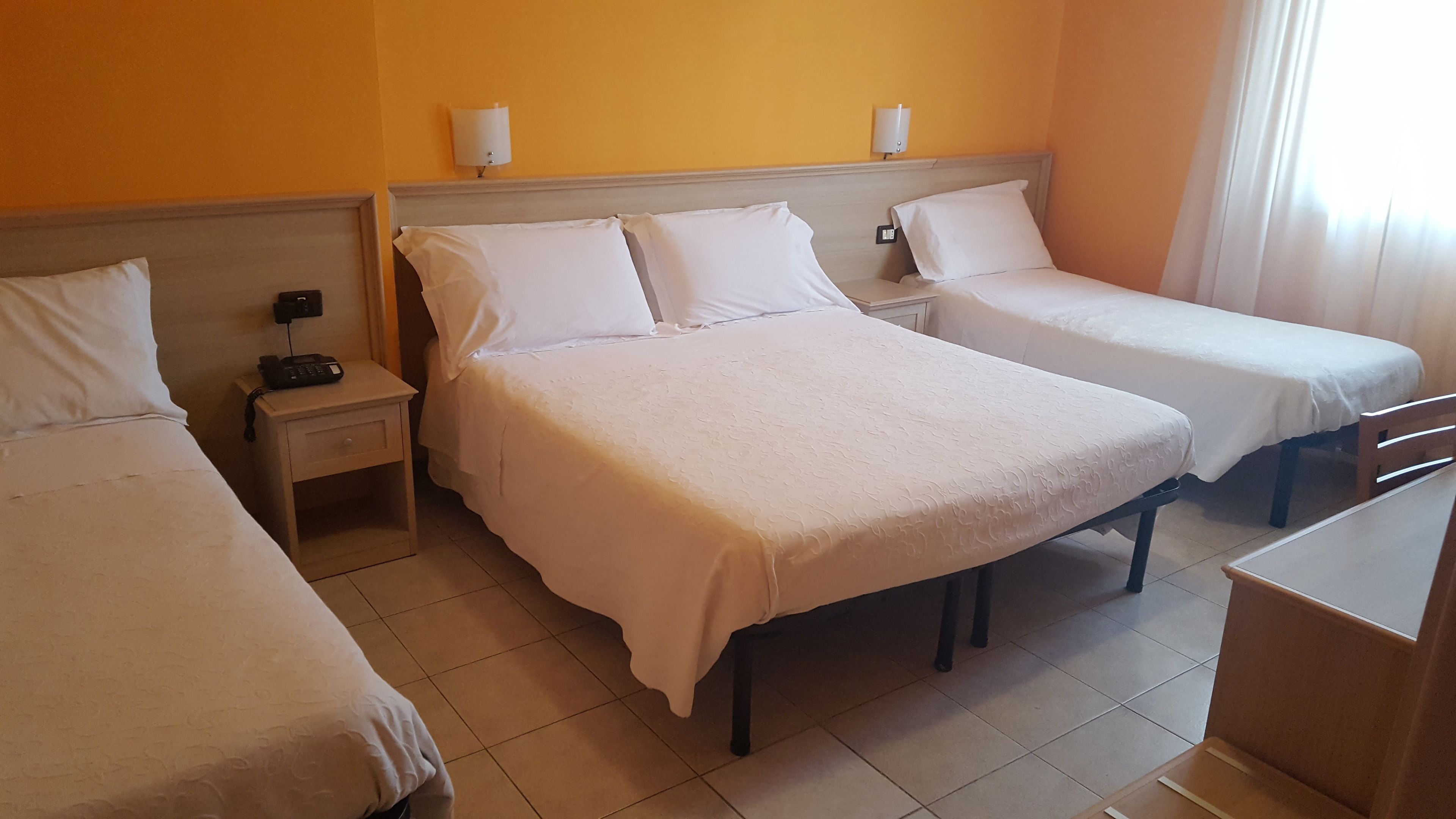 Una habitación de hotel con tres camas individuales, una mesita de noche pequeña con un teléfono y una silla.