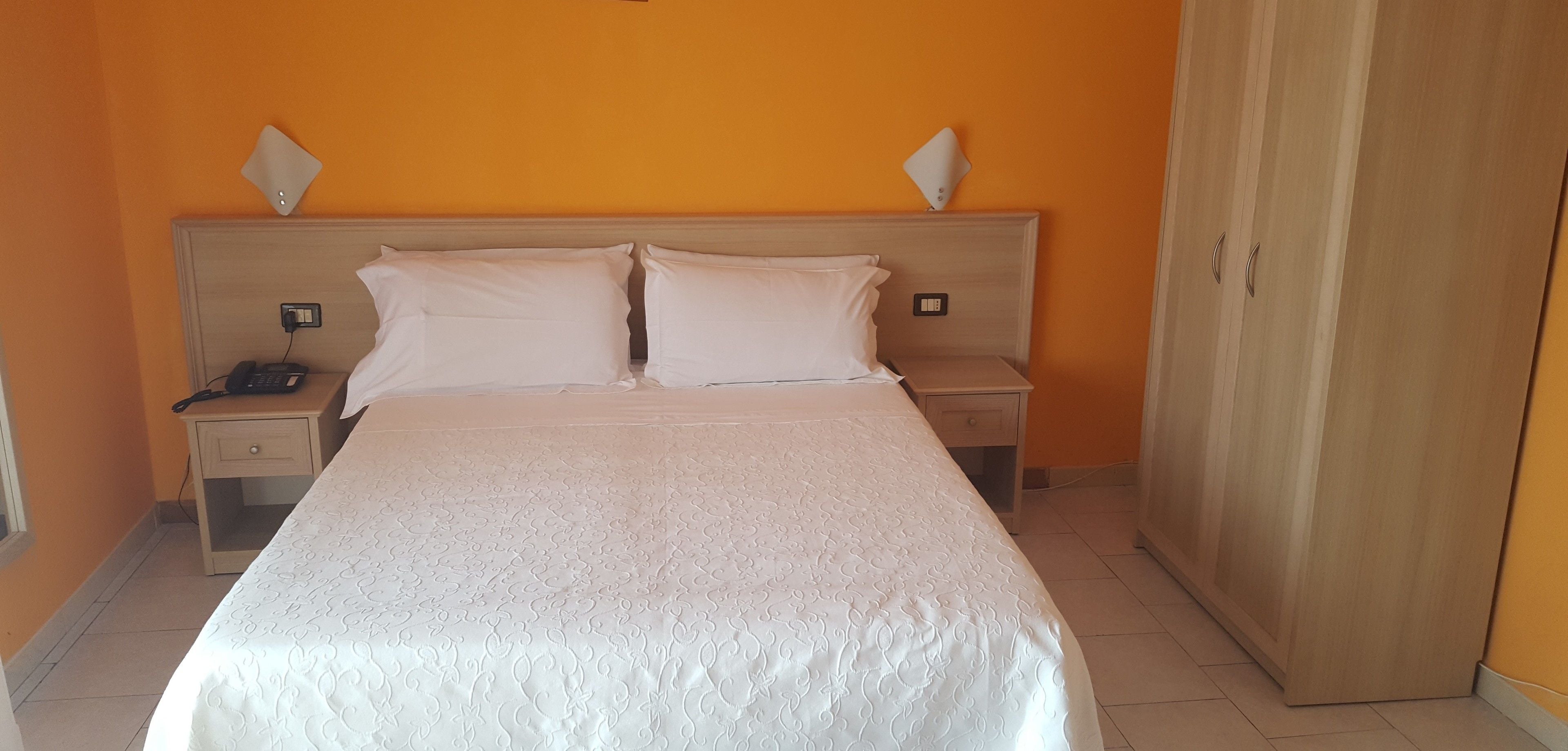 A hotel room with a bed, two bedside tables, a wardrobe, and a telephone on one of the tables.