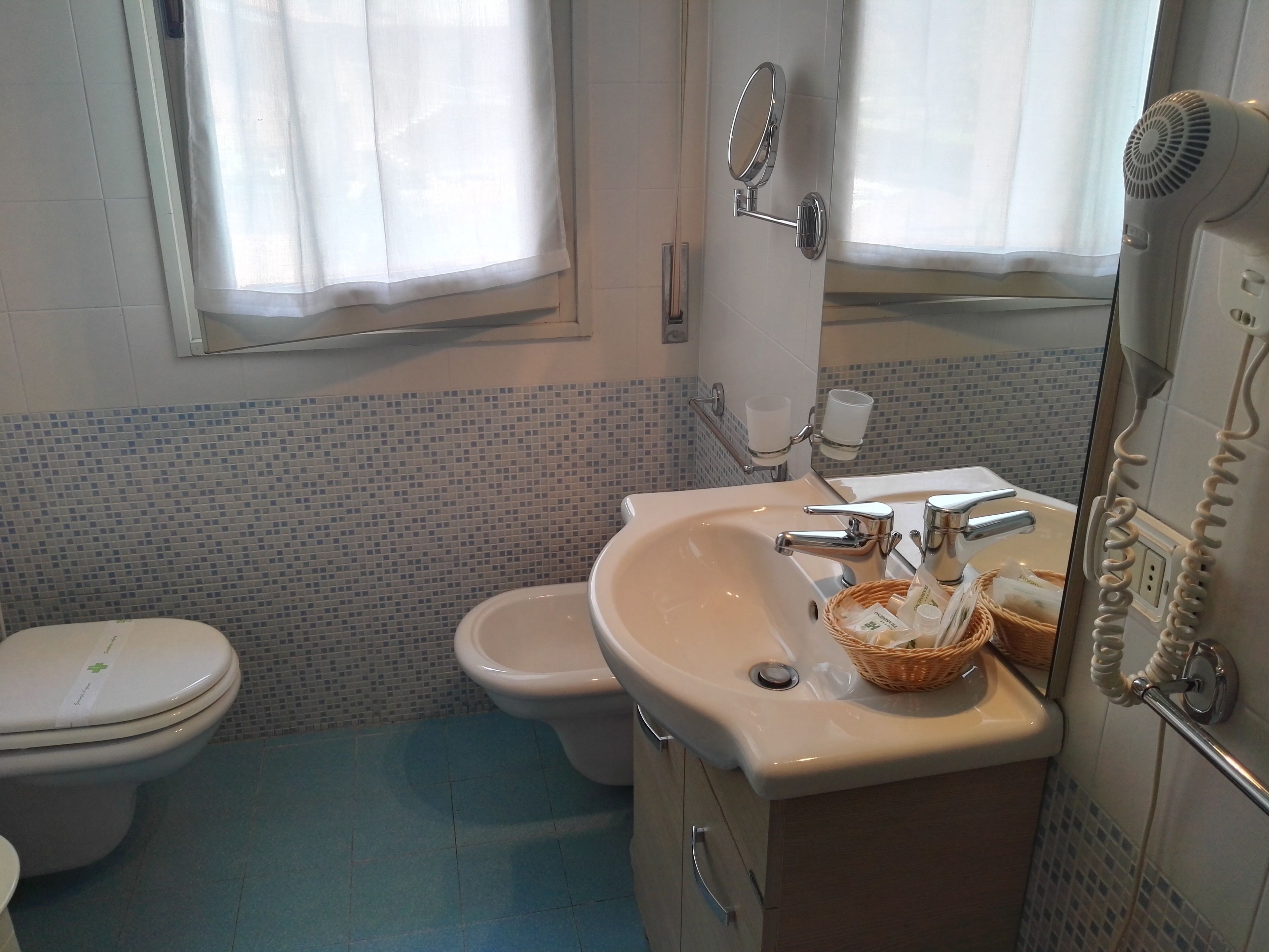 Une salle de bain équipée de toilettes, d’un lavabo, d’un miroir et d’un sèche-cheveux.