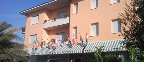 A hotel with a flat roof, multiple balconies, and a row of flags.