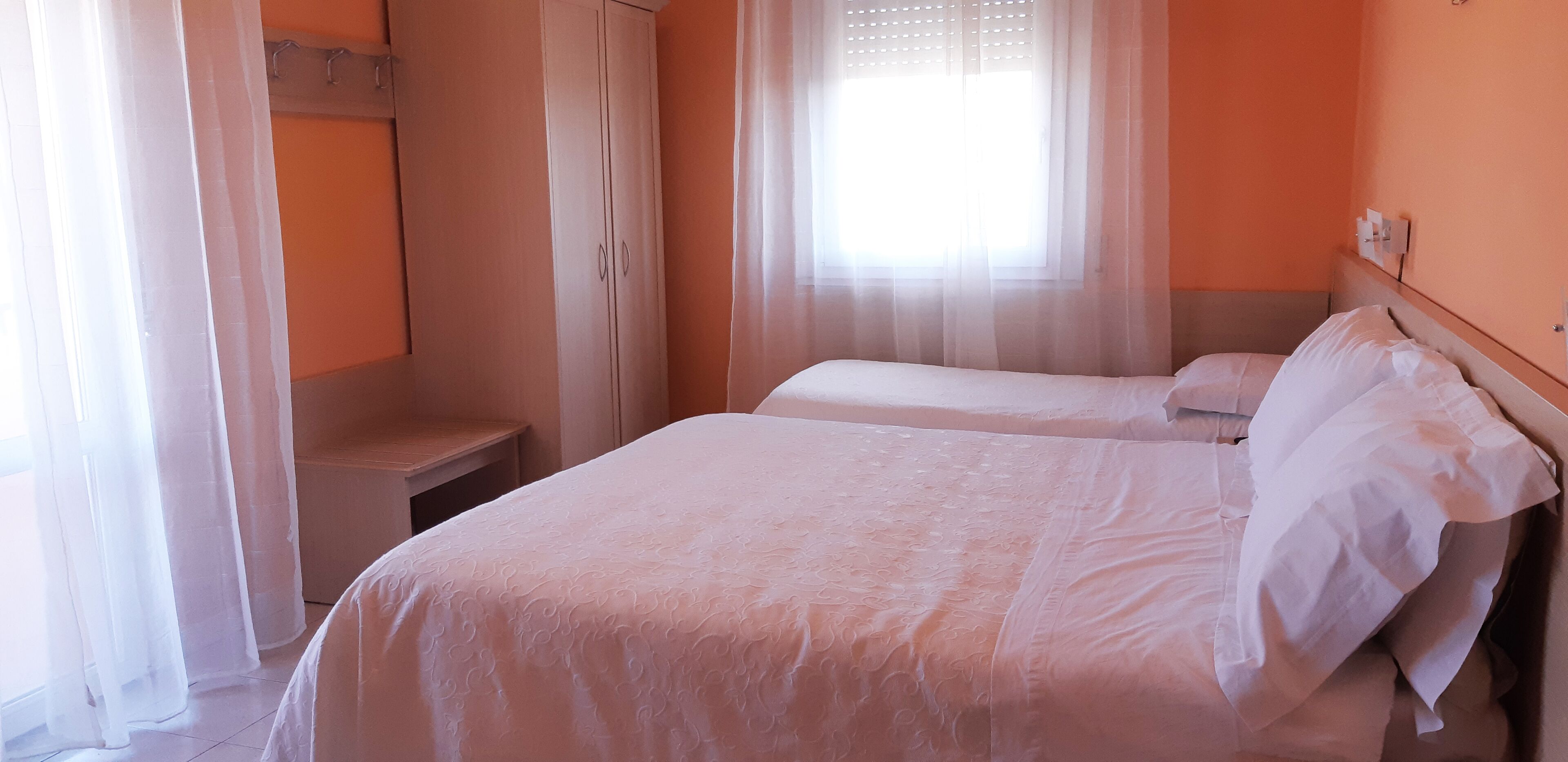 A bedroom with two beds, a wardrobe, and a window with sheer curtains.