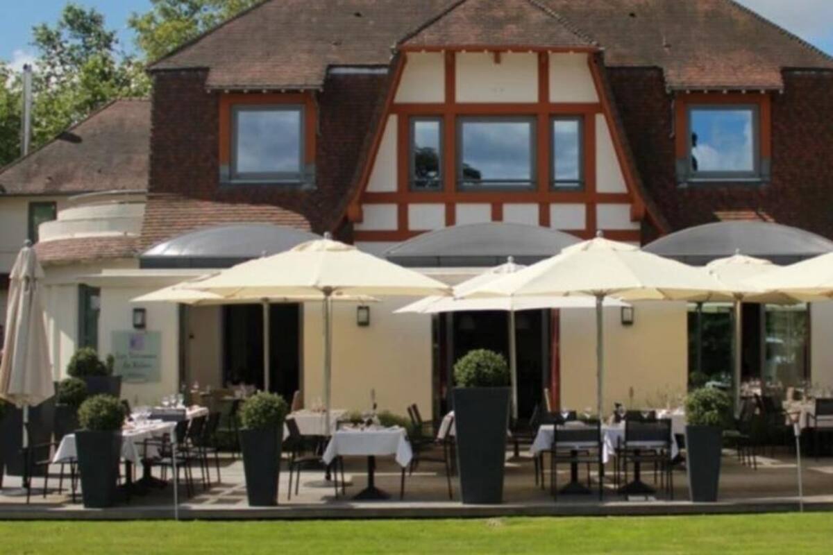 Een gebouw in traditionele bouwstijl, met een puntige kap en een bakstenen gevel. Er staan buiten tafels en parasols, wat wijst op een eetgedeelte.