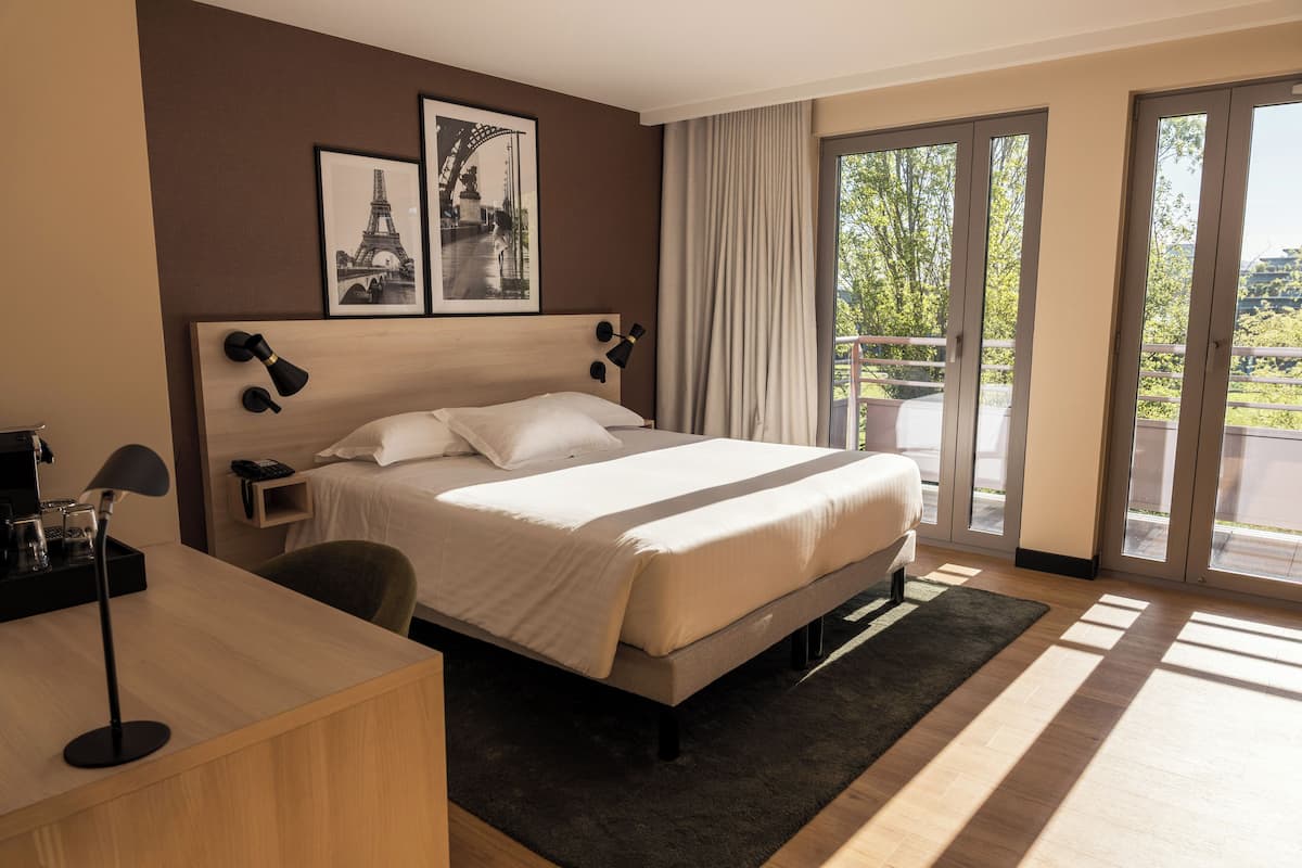 Een hotelkamer met een bed, een bureau, een stoel, een nachtkastje, een lamp en twee ingelijste foto's aan de muur.