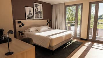 Une chambre d’hôtel comprenant un lit, un bureau, une chaise, une table de chevet, une lampe et deux tableaux encadrés accrochés au mur.