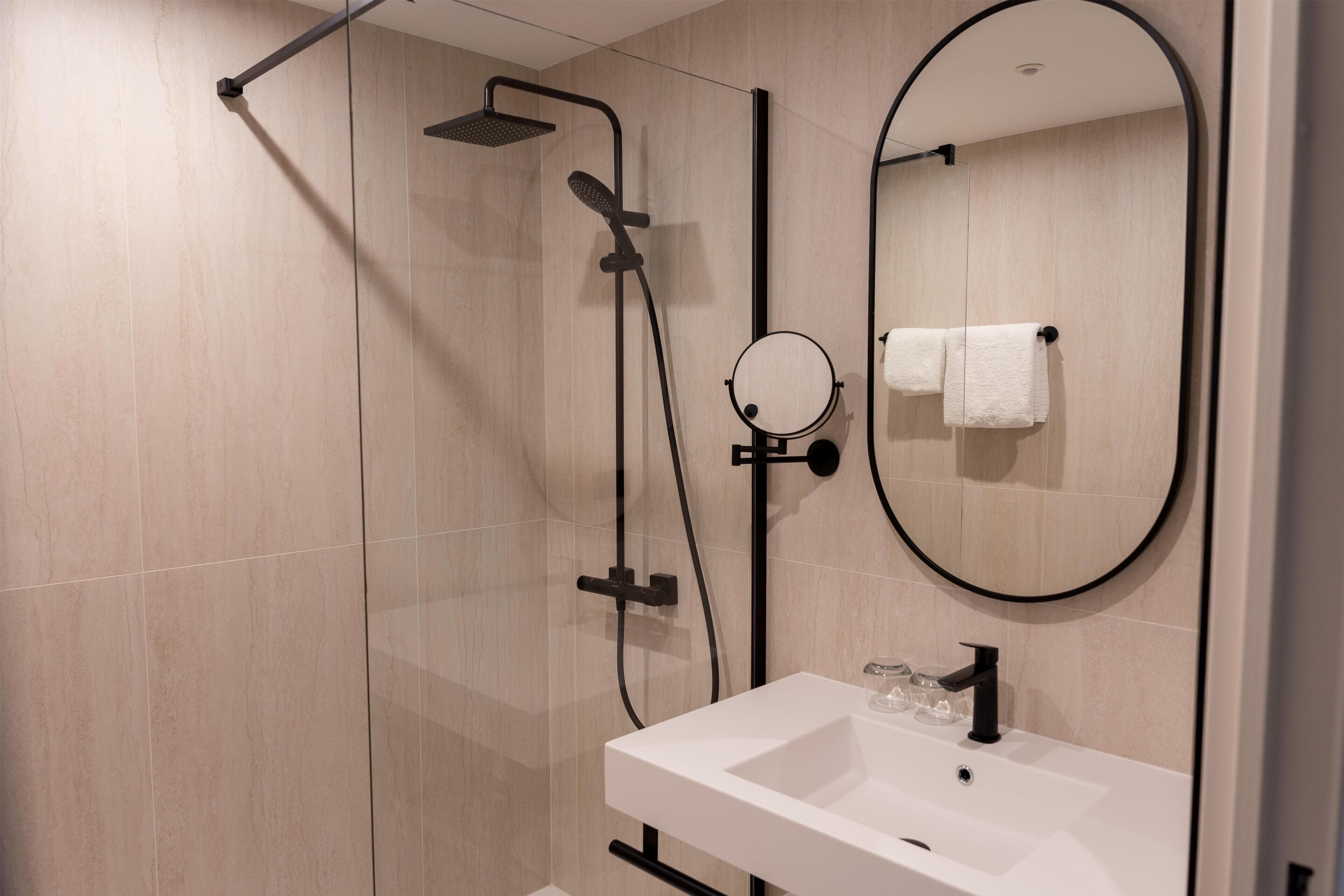 Un baño moderno con cabina de ducha de vidrio, un lavabo blanco y un espejo redondo.