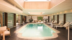 Une piscine intérieure moderne dotée d’une verrière, de chaises longues et d’un espace salon.